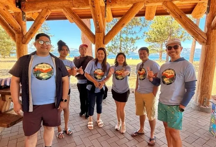 Team members in matching retreat shirts under a wooden pavilion, the lake behind them